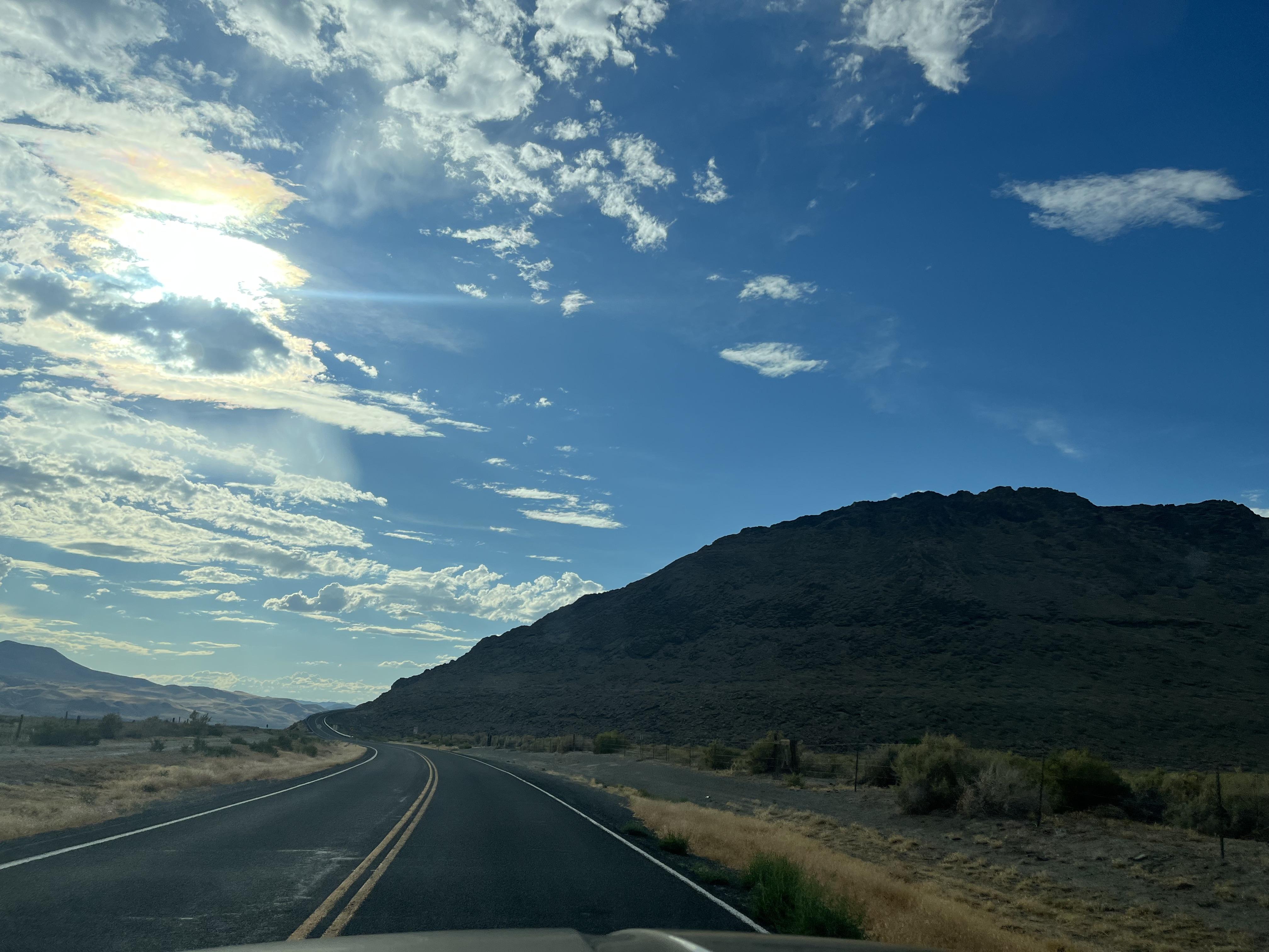 a road on the way to black rock city, open blue sky with clouds on the left, big hill rock on the right